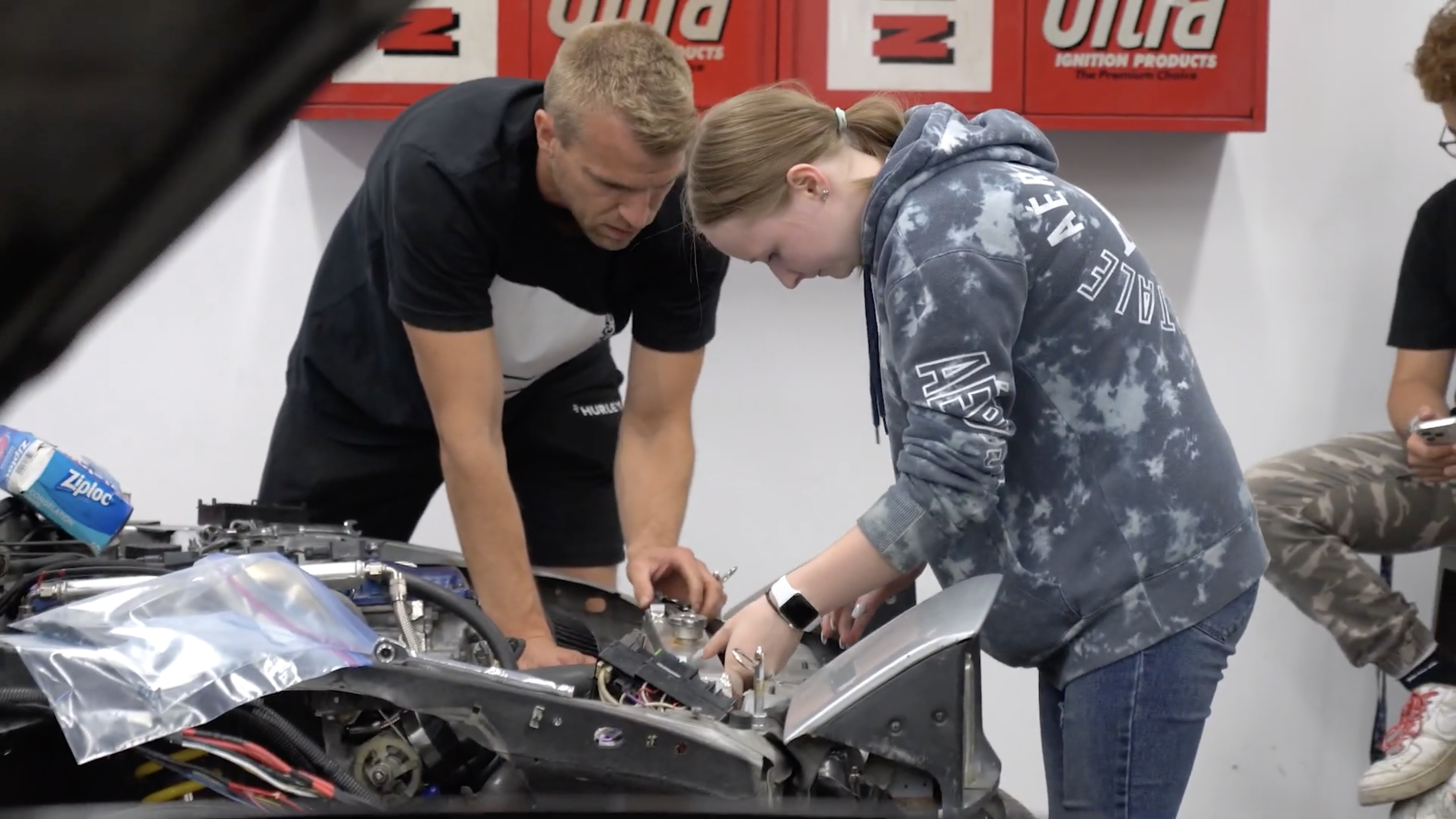 Two people working together on a car engine, side by side